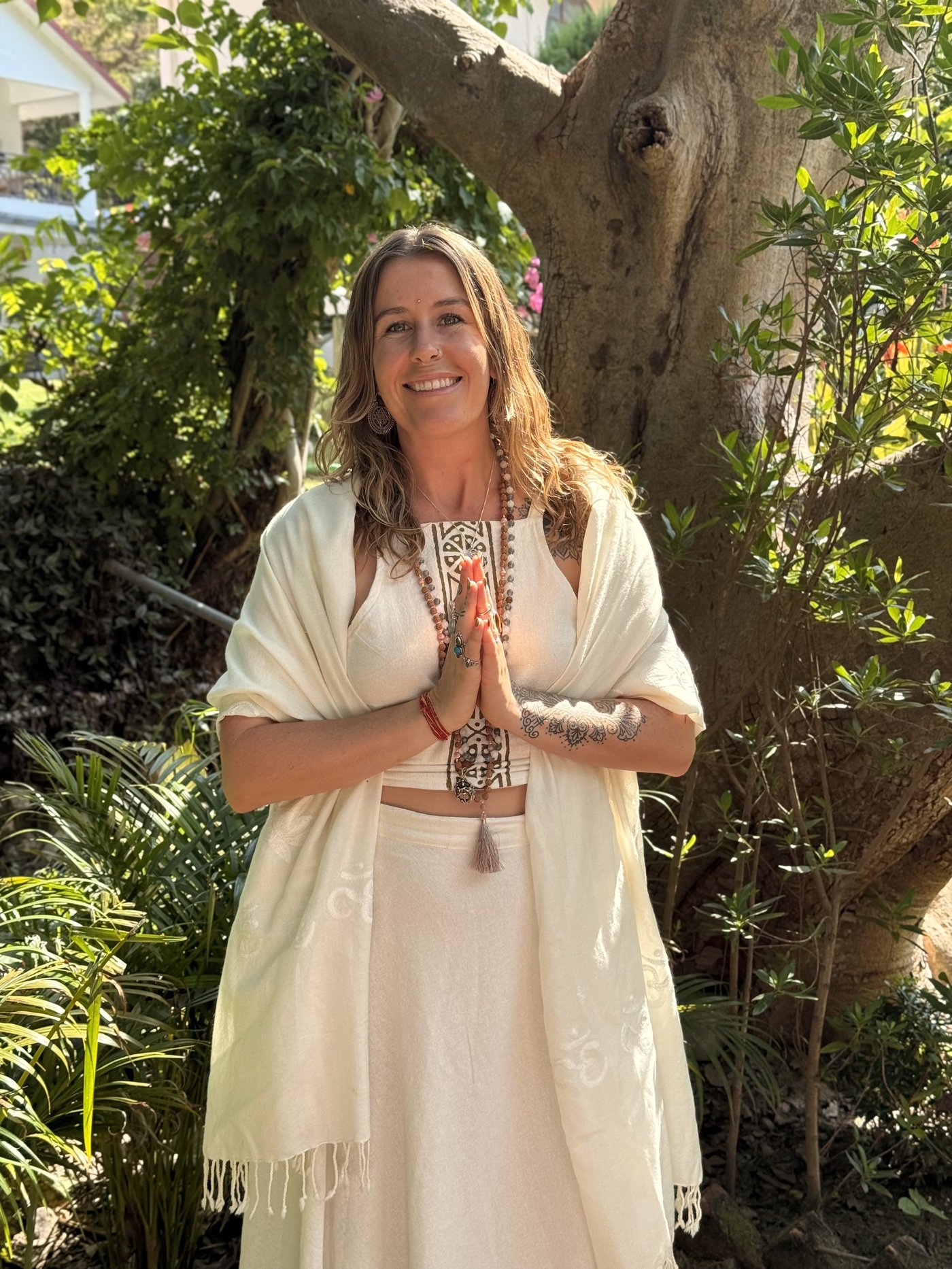 Cassidy smiling in prayer pose beneath a tree