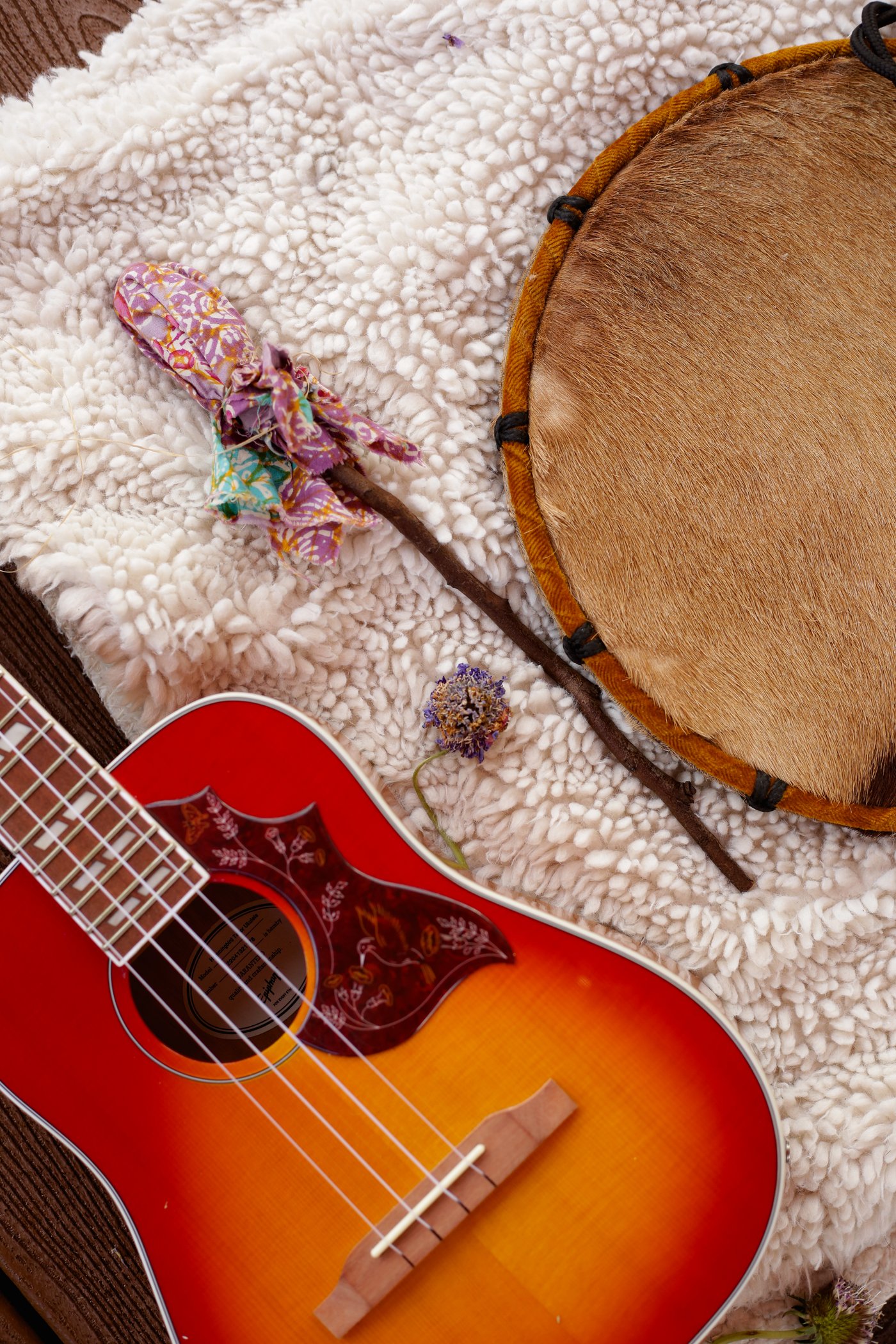 Ukulele, frame drum, and a handmade rattle laid out on a sheepskin rug